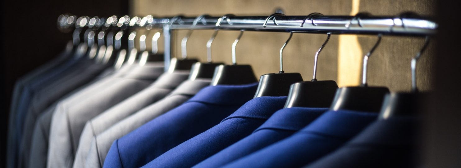 Blue, grey and black blazers on a clothing rack.