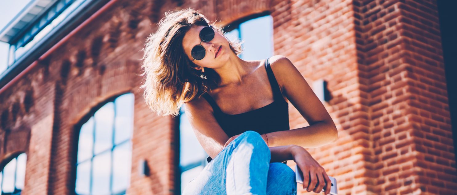 Lifestyle editorial photo of a women in front of a brick building with windows.