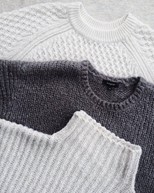 Three sweaters, two are white and one is dark grey. All three have different knitting patterns.