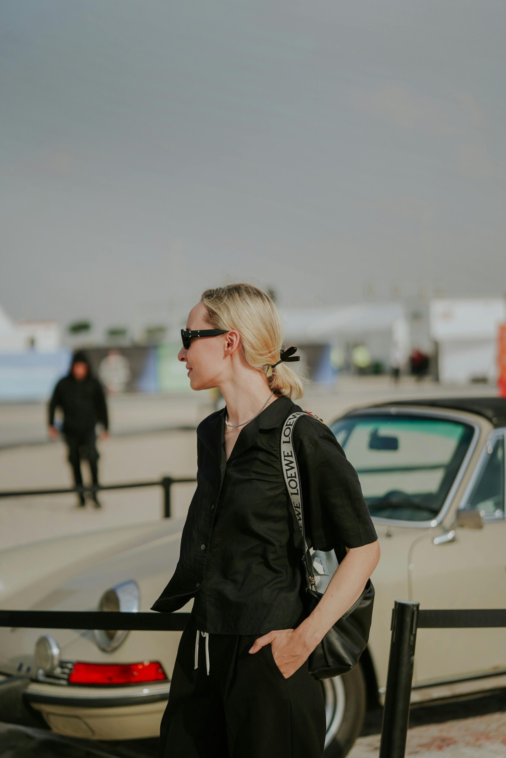 A women with blonde hair and a black outfit with a loewe bag around her arm